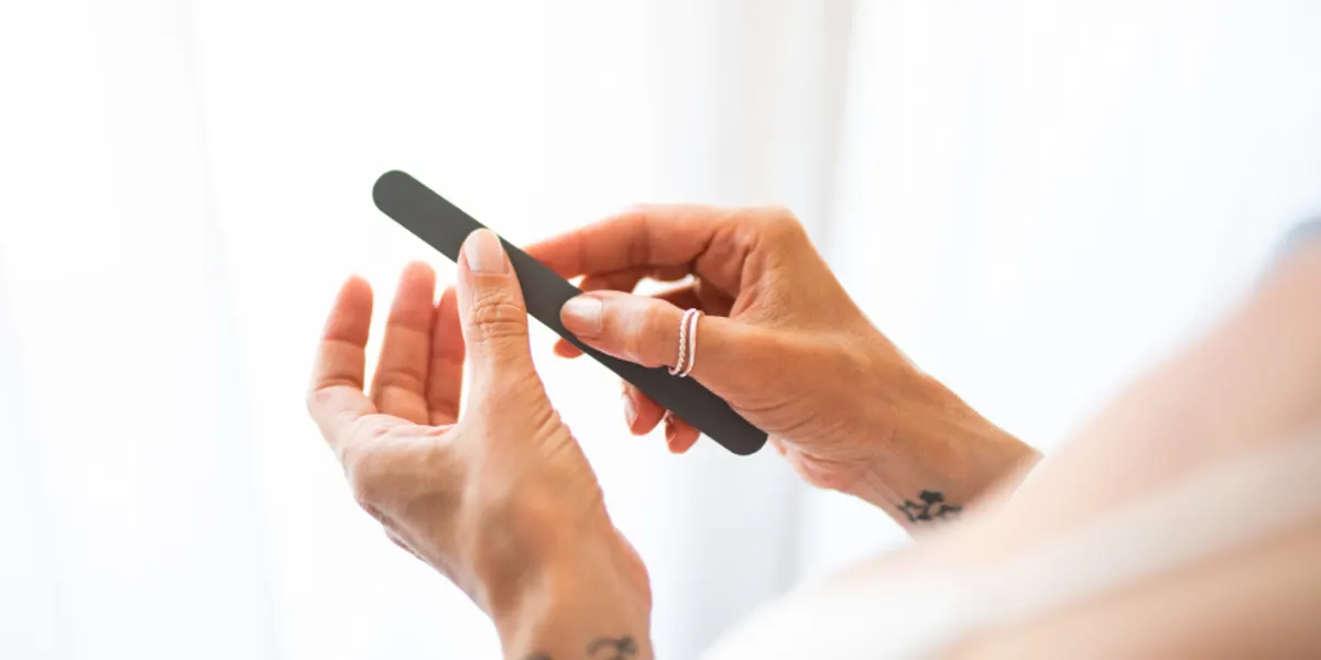 Hands holding a small nail tool to trim a nail